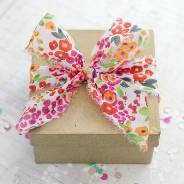 Colorful flower print fabric ribbon tied in a bow around a plain brown kraft gift box.