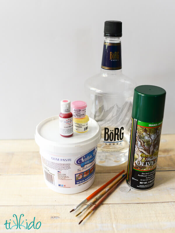 Materials for making basic gum paste flowers, including gum paste, food coloring, petal dust, vodka, and spray cooking oil.