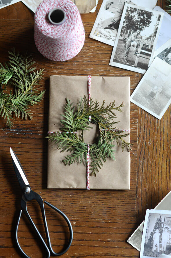 Package wrapped in brown paper, topped with a miniature wreath of real fresh evergreen and tied with red and white baker's twine.