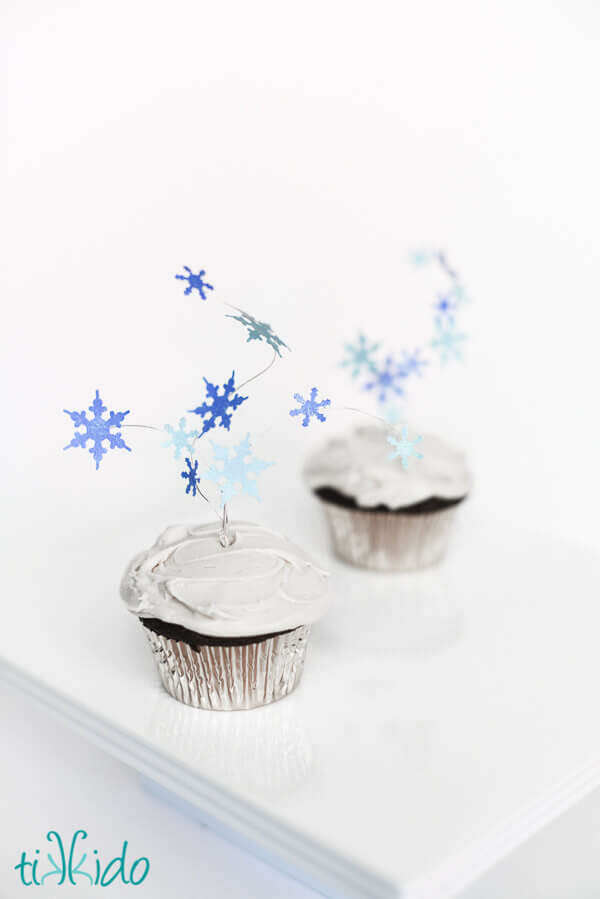 Two cupcakes topped with flying snowflakes cupcake toppers.
