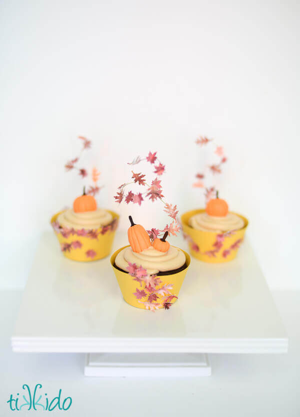 Three cupcakes topped with cupcake toppers that look like swirling fall leaves.