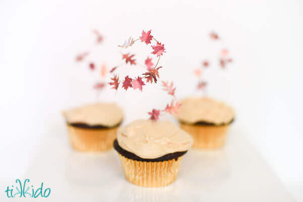 three cupcakes topped with swirling fall leaf cupcake toppers.