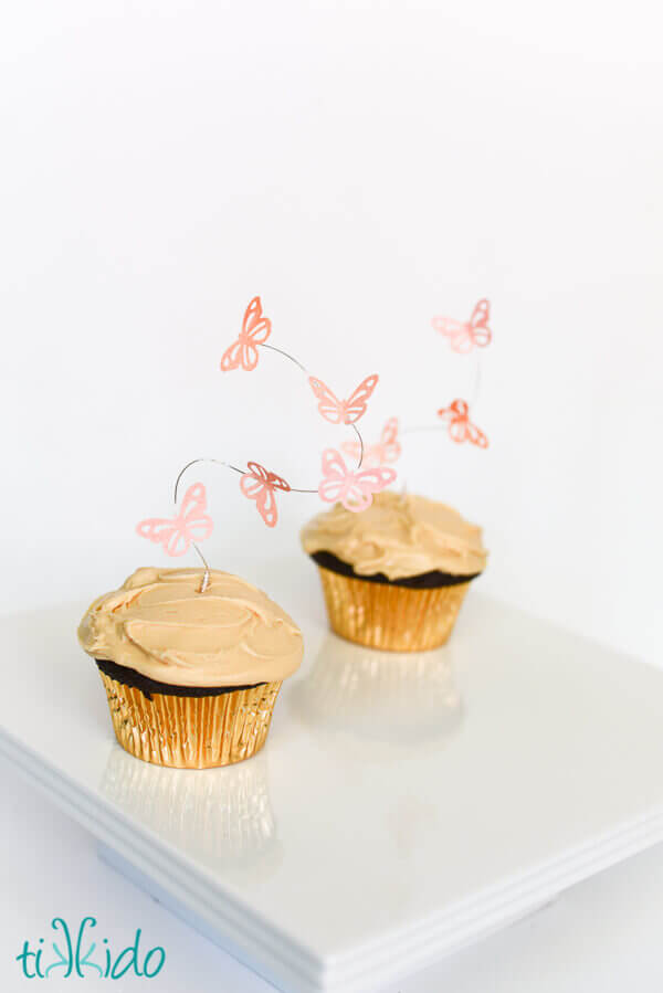 Two cupcakes topped with flying butterfly cupcake toppers