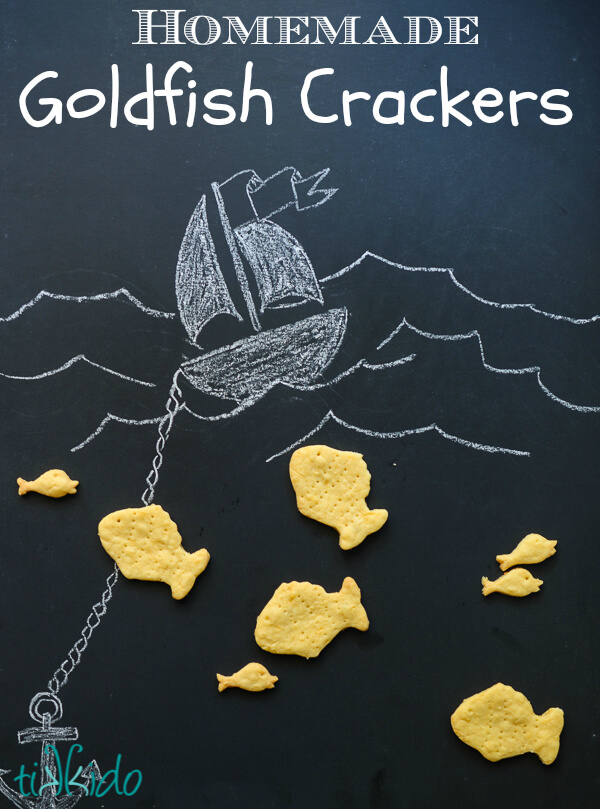 Homemade goldfish crackers on a black chalkboard background with a drawing of a boat and ocean waves.