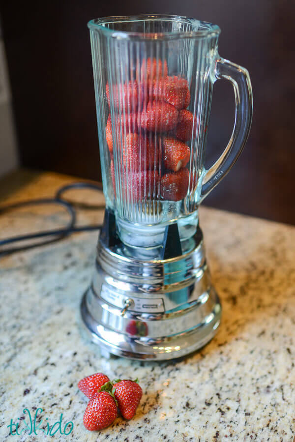 Strawberries in a waring blender on a granite counter.