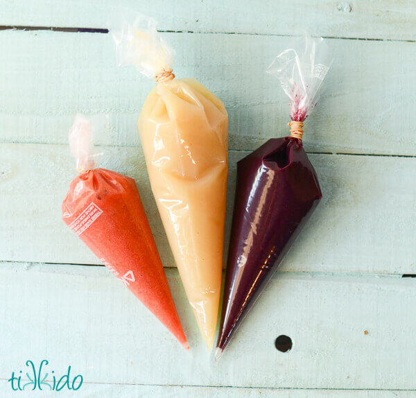 Three disposable piping bags filled with strawberry puree, applesauce, and blueberry puree.