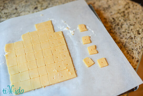 Square shaped Cheese crackers cut on a sheet of parchment paper.