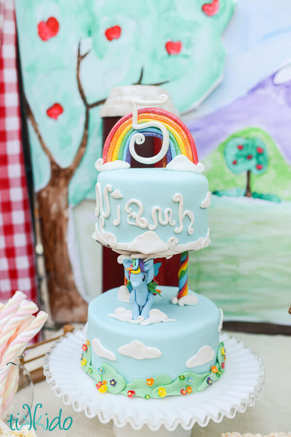two tier My Little Pony cake with a gum paste rainbow cake topper, and rainbow dash holding up the top tier.