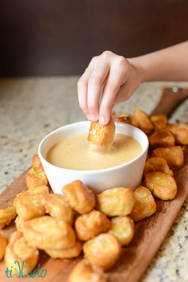 Hand dipping a homemade pretzel bite into a white bowl full of homemade beer cheddar dipping sauce.