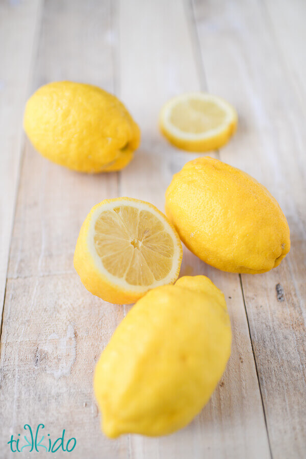 three whole lemons and one sliced lemon on a weathered white wooden surface.