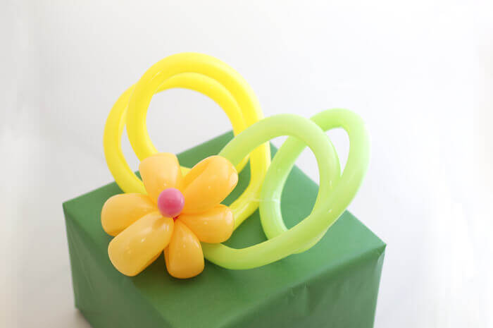 Present wrapped in green paper, topped with a twisted balloon flower.