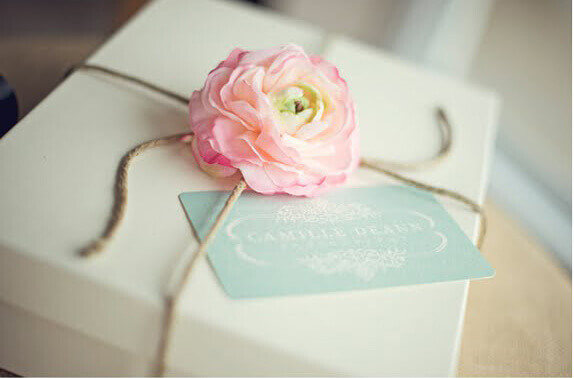 Plain white box tied with twine and topped with a pink silk flower.