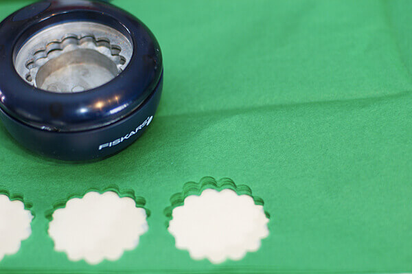 Scalloped circle paper punch on stacks of green tissue paper with three holes cut out.