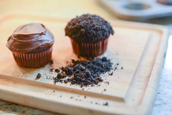 Two cupcakes covered in chocolate frosting and crushed Oreo edible dirt.