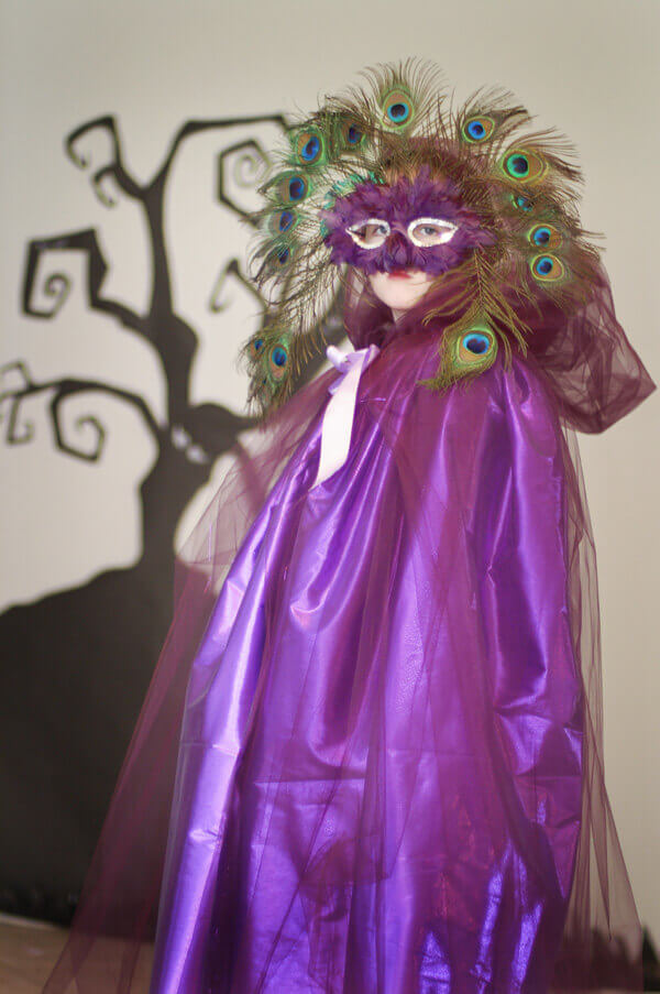 Little girl wearing a purple tulle cape and mardi gras masquerade mask.
