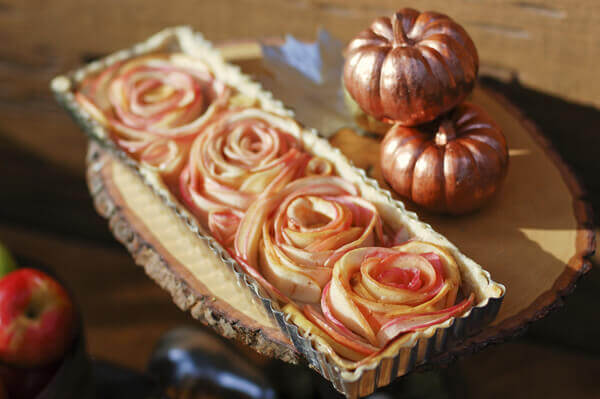 Rose Apple Pie on a wooden cake stand next to fall pumpkins.