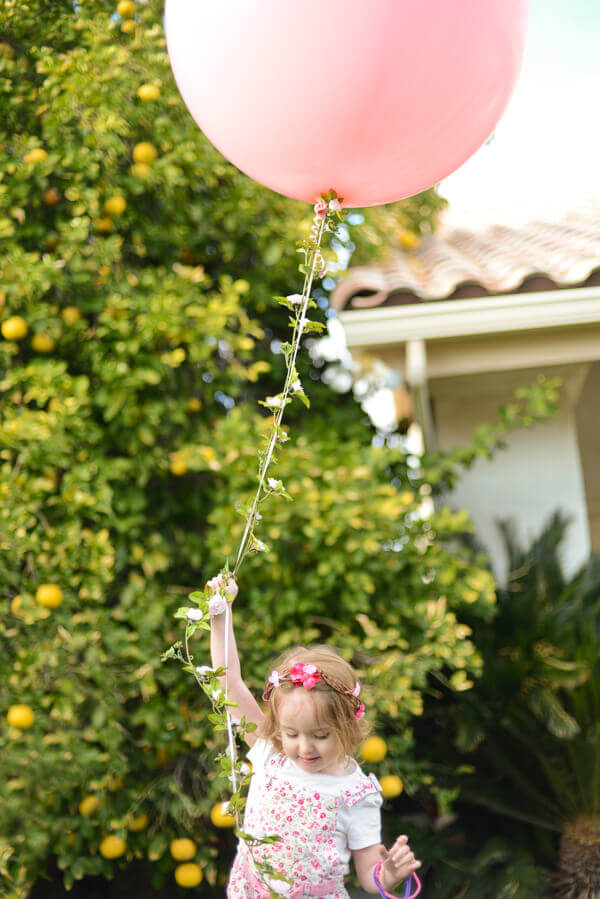 Large round pink balloon with a floral garland string held by a small girl with a flower crown.