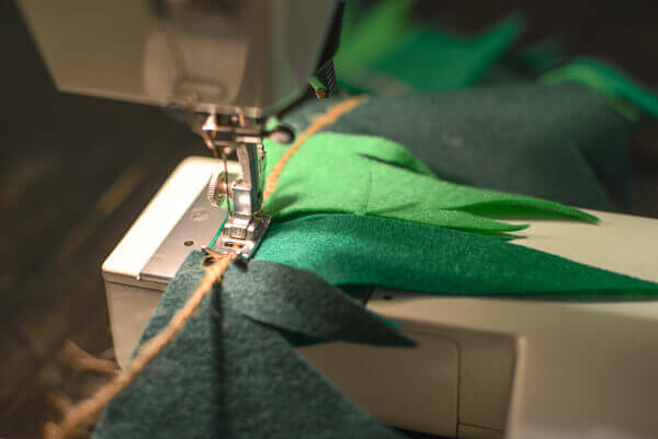 Green felt Peter Pan bunting being sewn to jute rope with a sewing machine.