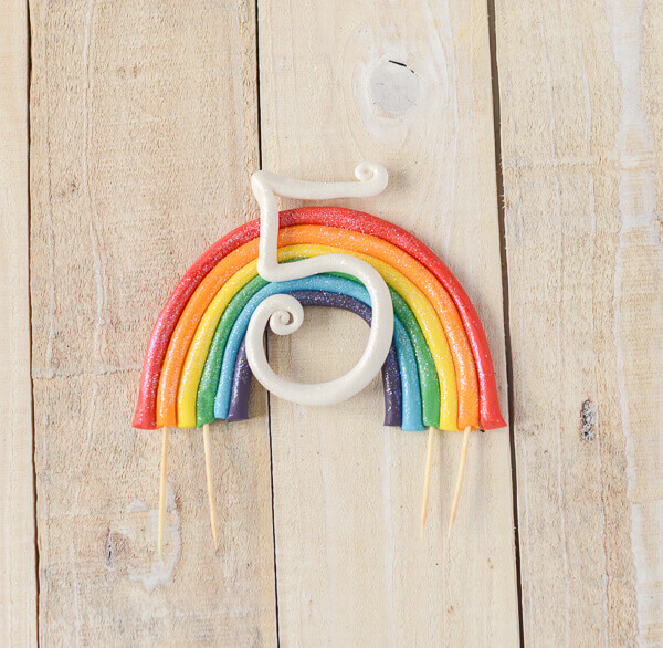 Simple rainbow cake topper made out of gum paste on a wooden background.