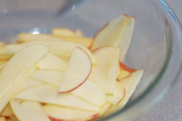 Thinly sliced apples in a clear bowl for Rose Apple Pie