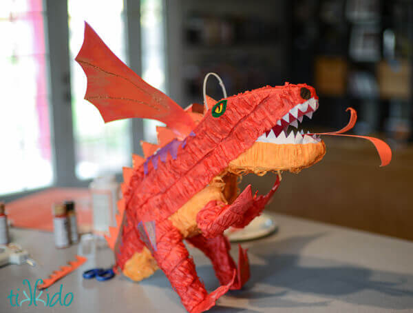 Attaching wings and other embellishments to dinosaur piñata to transform it into a DIY Dragon piñata.