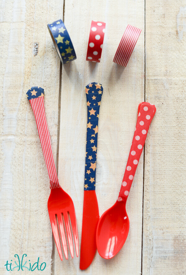 Three rolls of patriotic washi tape next to a red plastic fork, knife, and spoon with handles decorated with the washi tape.