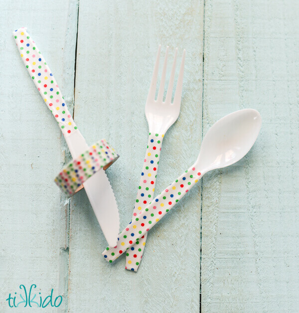 White plastic knife, spoon, and fork with handles decorated with rainbow polka dot washi tape.