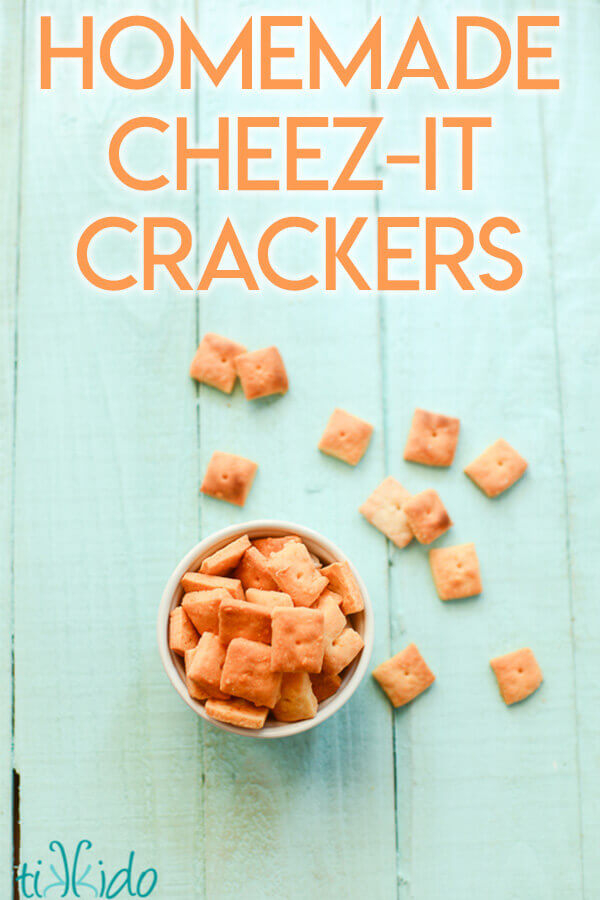 Homemade cheese crackers cut into tiny squares on a turquoise wooden background.