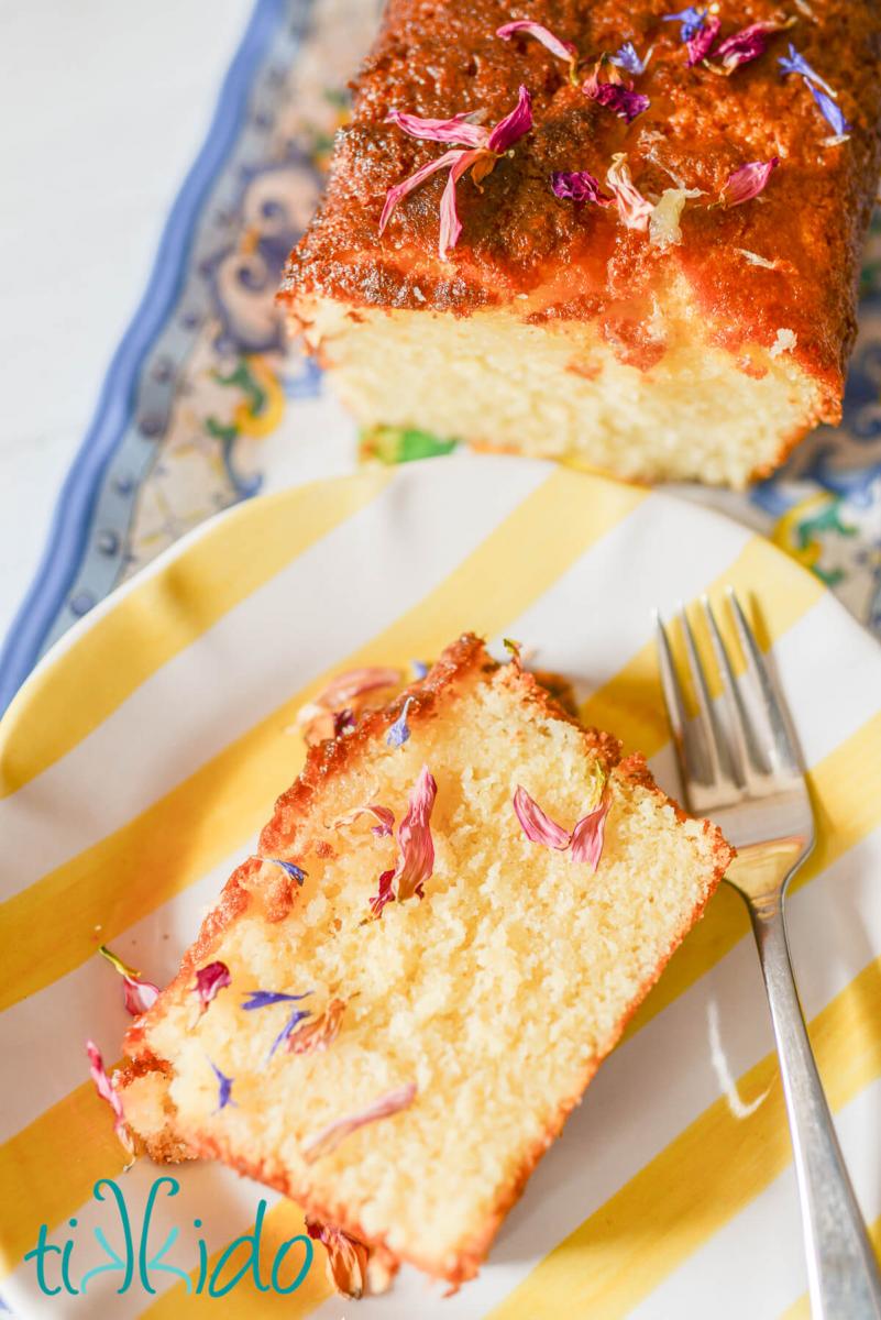 edible dried flower petals Slice of lemon drizzle cake decorated with dried flower petals, on a yellow and white striped plate with a fork next to the cake. You can just see the sliced loaf of lemon drizzle cake in the background.