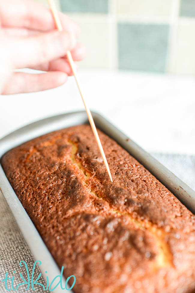 Freshly baked lemon loaf cake being poked with a bamboo skewer to help the lemon glaze soak in.