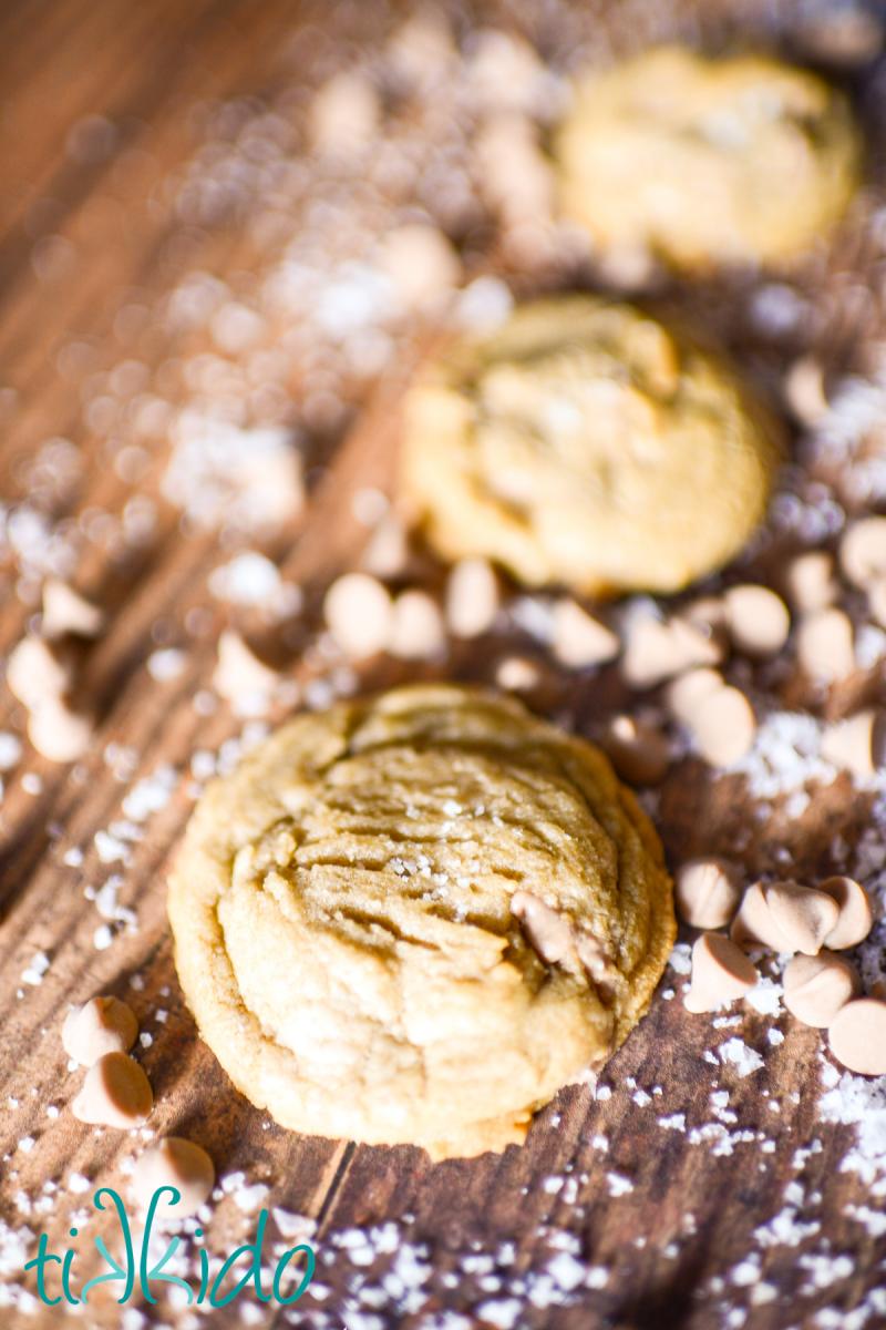 Salted Caramel Cookies Salted caramel cookies on a wooden surface, surrounded by salted caramel baking chips and flakes of sea salt.