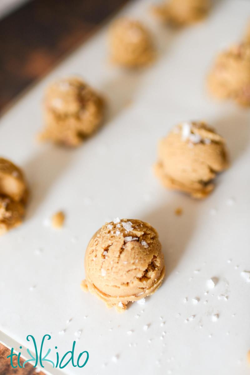 Salted Caramel Cookies Unbaked salted caramel cookies sprinkled with sea salt flakes and ready to be put in the oven on a parchment lined cookie sheet.