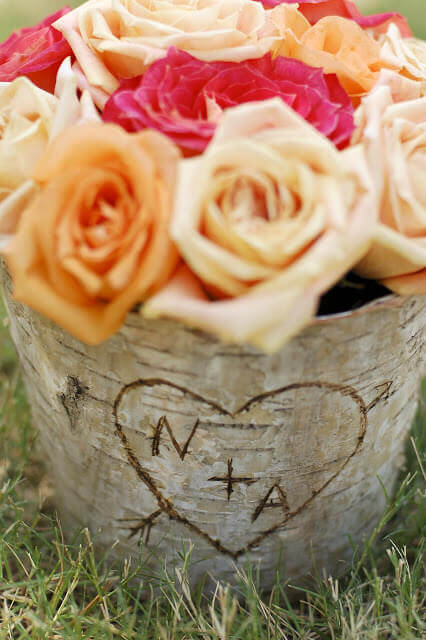 Birch bark covered zinc floral container filled with orange roses with the letters N + A in a heart carved into the bark.