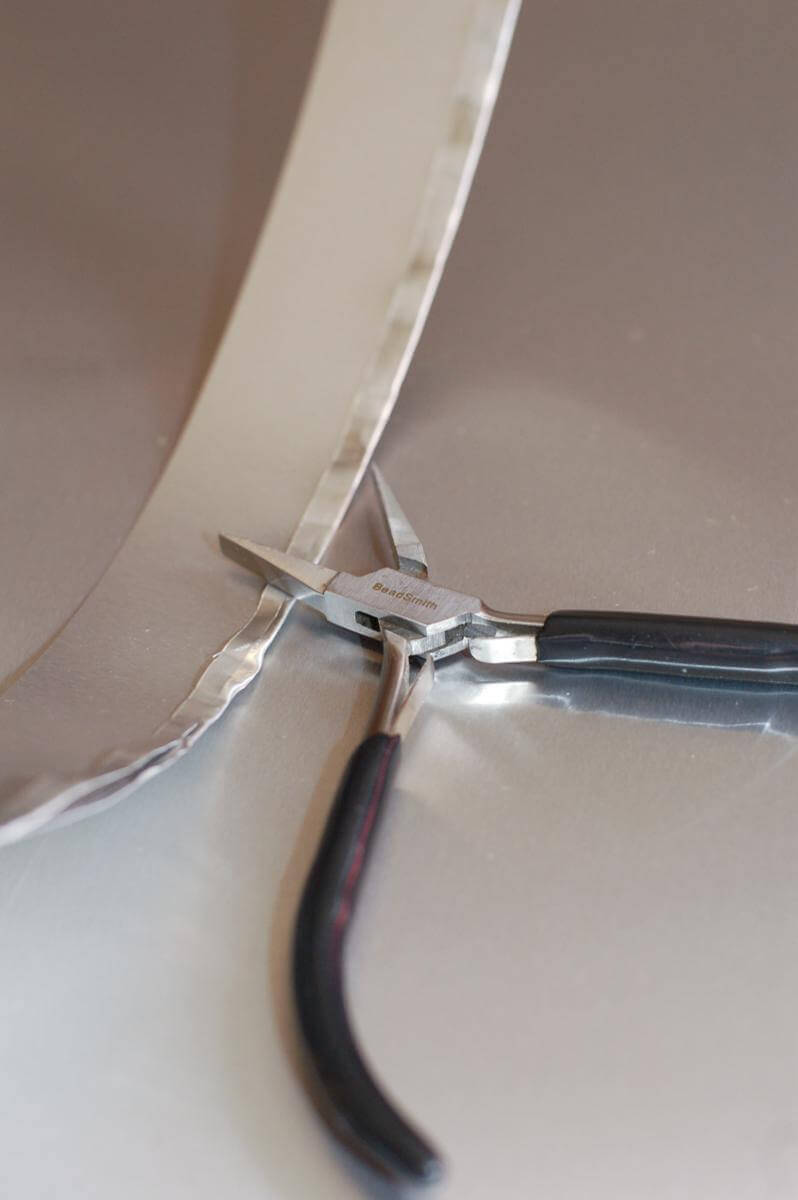 Jewelry pliers pinching over the raw edge of a strip of aluminum to make a cookie cutter.
